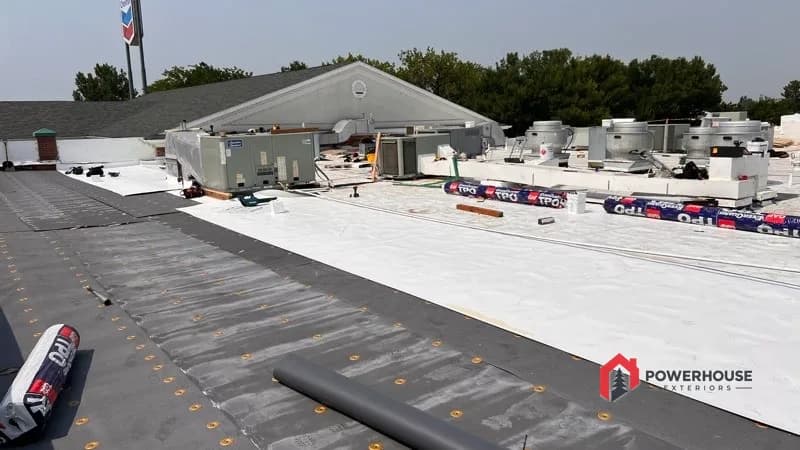 TPO membrane installation over a fastened cover board on the commercial hotel roof, with GAF rolls staged