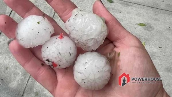 Golf-ball-sized hailstones held in a hand beside the damaged commercial roof