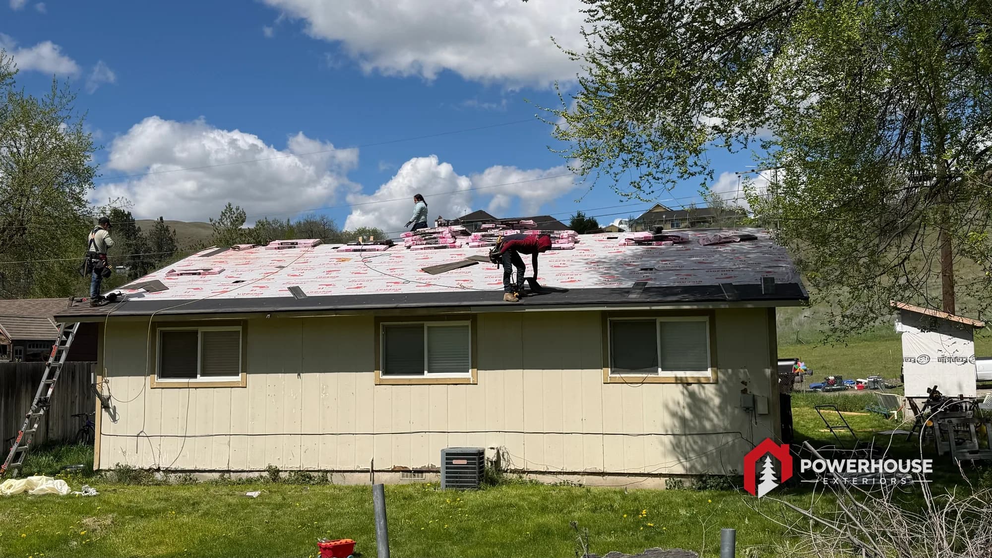 Roofing crew installing architectural asphalt shingles with bundles staged across a Boise roof